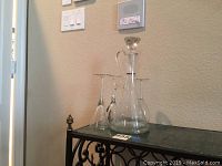 Photo of 2 glass decanters on a metal stand with 6 stem glasses around.
