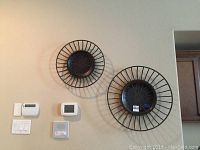 Two circular black metal wall art pieces mounted on wall, one larger (26 inch) and one smaller (20 inch) with radiating spoke design and patterned centers.