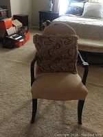 Side chair front view with beige upholstered seat and back, black wooden arms and legs, brown paisley patterned pillow with fringed edges