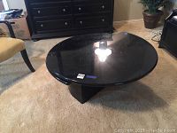 Full view of round black coffee table with glossy surface and solid base.