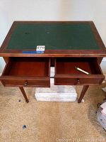Top view of small wooden desk showing two open drawers and green leather-like writing surface with slight wear.