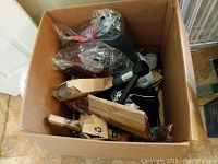 Photo of a large cardboard box containing various components and parts of exercise equipment, still in plastic packaging and boxes, indicating new and unassembled condition.