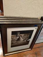 Stacked framed artworks resting against a wall, showing at least one framed piece with an abstract face and eye design.