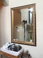 Frontal view of the mirror hanging on textured beige wall. Shows clear reflection and detailed ornate frame.