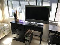 Black wooden desk with a Sony flat screen TV on top, an Acer computer tower and keyboard underneath, near a window with sunlight.