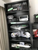 Full shelf view showing Panasonic boombox on top, Sony clock radios, Panasonic CD stereo, and surge protector with adapters.