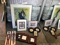 Variety of framed artworks and decorative plates arranged on floor, includes Aboriginal art by Alvin Adkins.