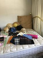 View of assorted hats including woven straw hats, felt hats in various colors, and knit beanie along with multiple scarves on bed