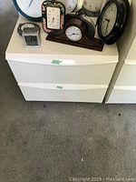 Front view of one nightstand showing two closed drawers with green tape and clocks/items on top