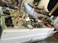Wide view of dresser top showing many items including sunglasses, perfume bottles, costume jewelry pieces displayed on trays, mirrors, and hair bows.