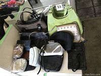 Photo showing multiple purses and handbags arranged on a white surface, highlighting large green handbag, black leather handbags, and various smaller pouches in different materials and colors.