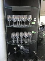 Wide view of glass cabinet shelves displaying two sets of wine glasses and additional small glasses on the bottom shelf.