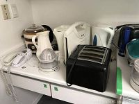 Black four-slice toaster, ceramic crock pot, citrus juicer, coffee carafes, and corded telephones on a white shelf.