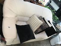 Photo showing the entire bone white leather love seat with four throw pillows in assorted colors and patterns.