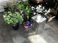 Photo showing group of faux plants in various pots along with mirrored pedestal on carpeted floor