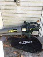 Side view of the Yard Works electric leaf blower and vacuum with attached reusable collection bag on the ground next to a house.