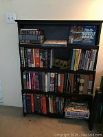 Front view of the black wood bookcase filled with various books on three shelves