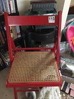 Red wooden chair with woven cane seat, showing some wear and discoloration.