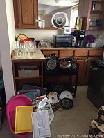 Wide shot of kitchen counter and shelves with toaster oven, coffee maker, pans, trays, and glassware arranged