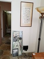 Three framed Asian style art pieces displayed: one vertical calligraphy, one vertical floral painting, one smaller floral print, with partial room background