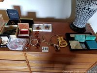 Overview photo of multiple pieces of costume jewelry including necklaces, pins in boxes, bracelets, and assorted items on a wooden surface.