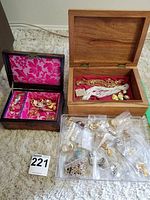 Photo showing two wooden jewelry boxes open with assorted jewelry inside and plastic container holding multiple small bags of clip-on earrings and jewelry pieces.