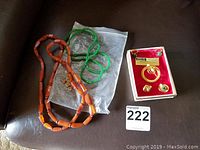Overview of all jewelry items including two necklaces with green and orange beads, a pair of clip-on earrings, and a brooch in red velvet box.