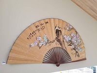 Large decorative Oriental folding fan hanging on wall, showing bird on branch with blossoms and Chinese calligraphy text