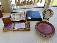 Group shot of six items: hexagonal porcelain dish, black lacquer tray, porcelain plate on stand, sliding-lid box with bowls, fabric-covered coaster box, wooden platter