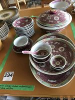 A photo showing large serving bowl with lid, multiple smaller plates and bowls with red, gold and green detailing, porcelain spoons, and small sauce cups.