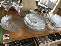 Wide view of clear glass dishes and some ceramic cups on table, showing assortment of bowls and platters in different shapes and textures