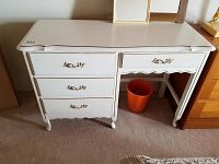 Front view of white desk with gold trim and three drawers, showing scratches and dings.