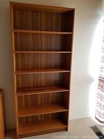 Full front view of wooden bookcase showing six shelves with woodgrain panels.