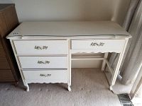 Front view of white four drawer desk showing drawer configuration and decorative gold-tone handles.