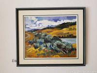 Framed oil painting of rolling hills with water body under cloudy sky