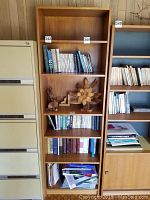 Frontal view of tall wooden bookshelf filled partially with books and decorative items.