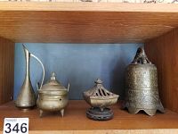 Front view of four metal decor items including tall bell, pitcher, lidded bowl, incense burner on shelf