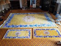 Large yellow and blue floral bordered area rug with central medallion, placed on patterned carpet in living room