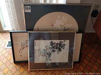Four framed Asian themed pictures arranged leaning on wall, showing variety of art styles and frame types.