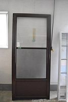 Full view of brown screen door showing the upper mesh screen and lower solid panel, with brown frame.