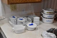 Overview of white CorningWare casseroles and French White dishes with lids and blue patterning, showing variety of sizes and shapes including square, rectangular, and round.
