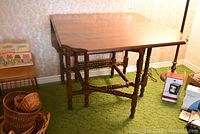Side view of the wooden drop leaf gate leg table showing the open leaf and turned legs on green carpet.