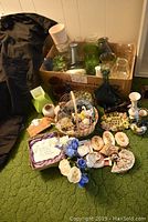 Overview photo of all vases and decorative items in and around a cardboard box on a green carpet with black fabric on side.