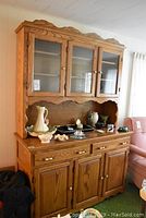 Frontal view of the oak buffet and hutch showing three glass doors on hutch and wooden drawers and doors on buffet with decorative edges.
