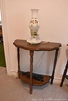 Wood demi lune table with hurricane lamp on top and black panther figurine on lower shelf.