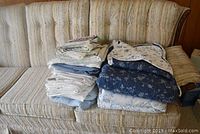 Stack of folded bedding including quilt, sheets, blankets, and comforter arranged on couch