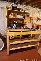 Wide view of wooden shelf unit with various household items and the boxed Fellowes paper shredder visible
