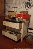 White wooden three drawer dresser with two drawers open and boxes of hardware and household items on top.