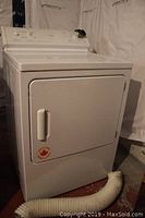 Exterior front view of dryer with door closed and vent hose on floor