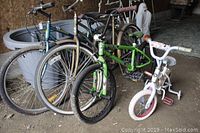 Photograph showing multiple bicycles including girls 9 inch, youths 12 inch, and ladies 20 inch bikes with different colors and sizes inside a garage or storage area.
